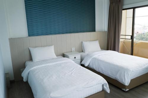a room with two beds with white sheets and a window at Baanthanam Nont in Nonthaburi