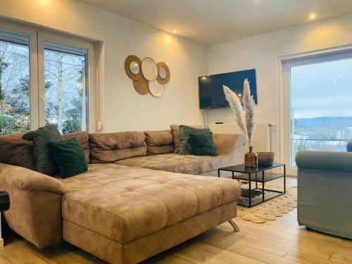 a living room with a brown couch and a large window at Maison de vacances privative à louer in Aywaille