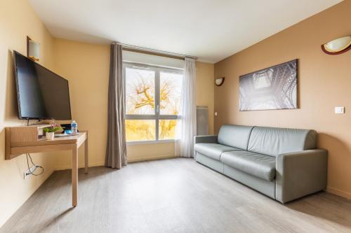 a living room with a couch and a television at Zenitude Hôtel-Résidences Magny-les-Hameaux in Magny-les-Hameaux