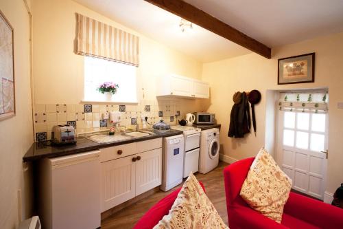 cocina con electrodomésticos blancos y sofá rojo en The Cottage at Weston Lawn en Bath