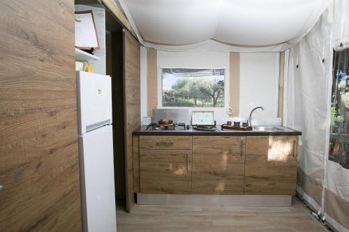 a kitchen with wooden cabinets and a white refrigerator at Ciriga Sicily Glamping Resort in Santa Maria Del Focallo