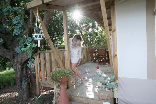a woman is standing on a wooden porch at Ciriga Sicily Glamping in Santa Maria Del Focallo