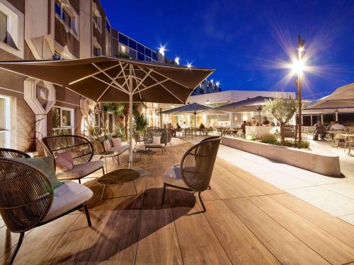 a patio with chairs and an umbrella and tables at Novotel Clermont-Ferrand in Clermont-Ferrand