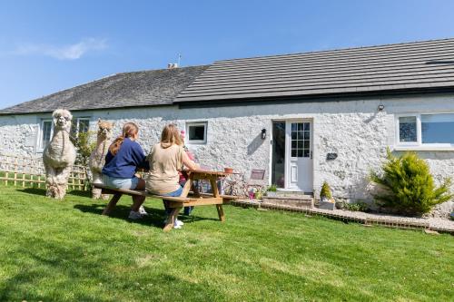 three people sitting on a bench in front of a building at South Barlogan Farm in Bridge of Weir