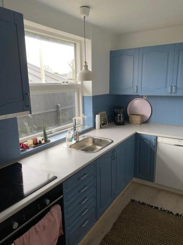 uma cozinha com armários azuis, um lavatório e uma janela em Emmas hus i Skagen em Skagen