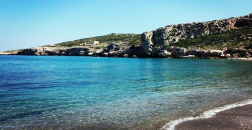 a beach with blue water and a hill in the background at Harmony in Lávrion
