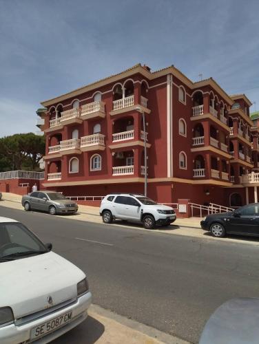 een rood gebouw met auto's ervoor geparkeerd bij Apartamento rojo con vistas al mar in Mazagón