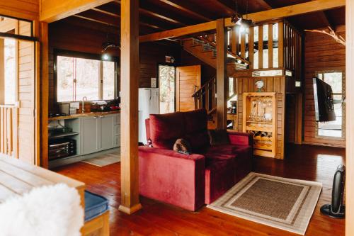 a living room with a red couch and a kitchen at Chalé Aconchego - Pousada Cachoeira da Neve in Urubici