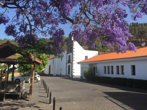 uma rua com um edifício branco e uma árvore com flores roxas em Casa Las Enanitas I - Casa Leo em Fuencaliente de la Palma