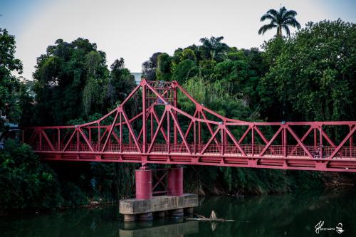 a red bridge over a river with trees at Hotel Village Cataguases in Cataguases