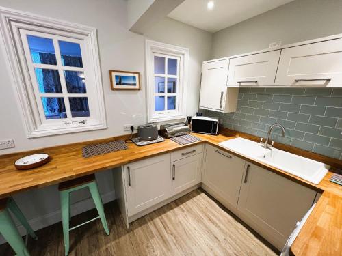 cocina con armarios blancos y encimera de madera en Orchard Cottage, en Ventnor
