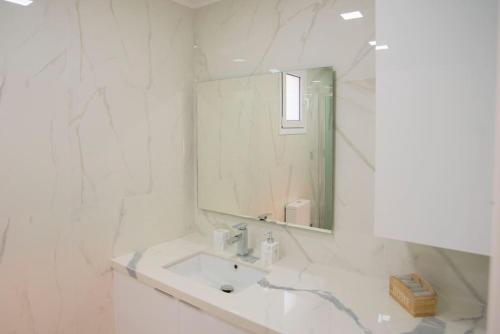 uma casa de banho branca com um lavatório e um espelho em Oniro Home em Ierápetra