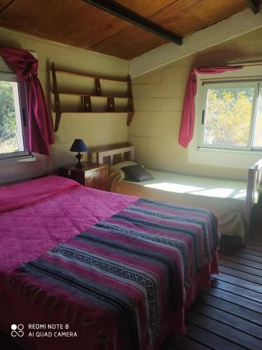 a bedroom with a large bed and two windows at Aike Cabañas de Montaña in San Clemente