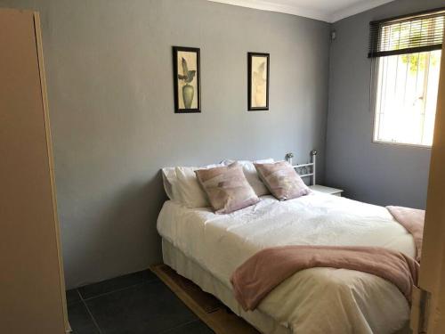 Schlafzimmer mit einem Bett mit weißer Bettwäsche und rosa Kissen in der Unterkunft Mels Place in Bloemfontein