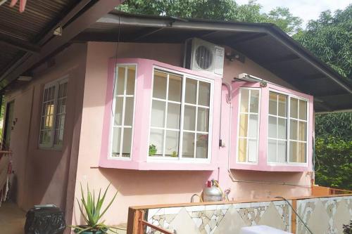 a pink house with white windows and a porch at Casita Independiente, Ubicada Atrás de Nuestra Casa in David