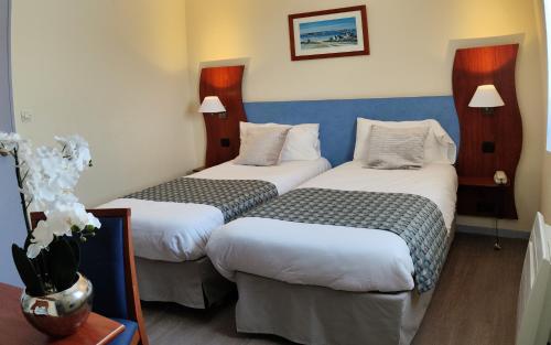 a hotel room with two beds and a vase of flowers at Hôtel Estuaire in Saint-Brevin-les-Pins
