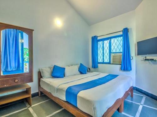 a bedroom with a bed with blue curtains and a window at Candolim Boutique House in Candolim