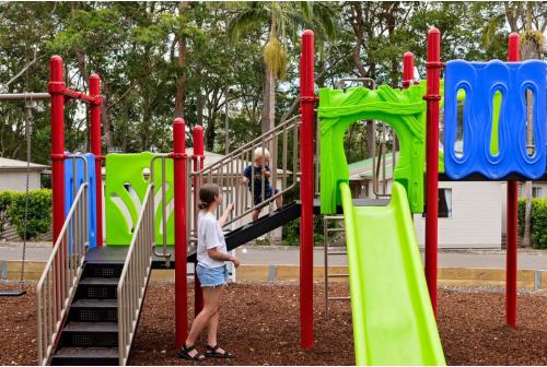 a young boy standing on a slide at a playground at Discovery Parks - Burrill Lake, Ulladulla in Burrill Lake