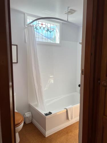 baño con bañera, aseo y ventana en The Old Vicarage en Reefton