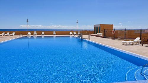 a large blue swimming pool with chairs and the ocean at Beach Apartment Poris in Poris de Abona