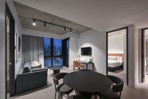 Nesuto Docklands في ملبورن: غرفة معيشة مع طاولة وكراسي وغرفة نوم
