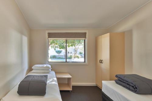 twee bedden in een kleine kamer met een raam bij NRMA Sydney Lakeside Holiday Park in Narrabeen