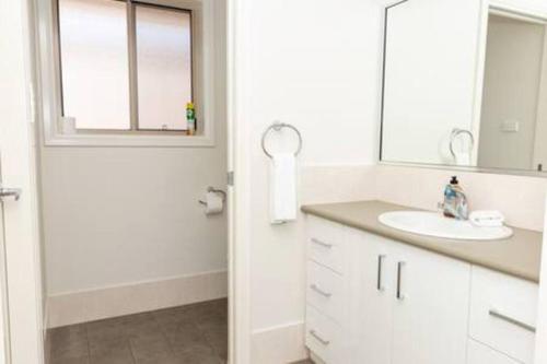 La salle de bains blanche est pourvue d'un lavabo et d'un miroir. dans l'établissement Lovely 3 Bed, 2 Bath in the City Centre!, à Wagga Wagga