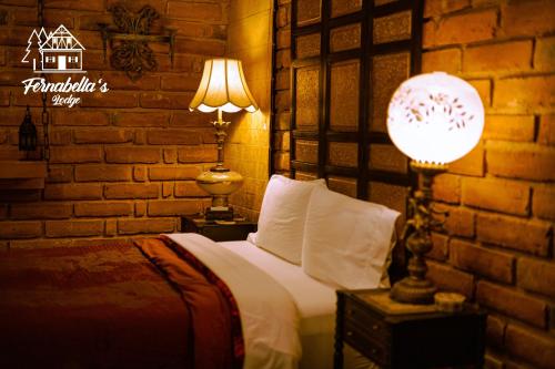 a bedroom with a bed with two lamps and a brick wall at Fernabella's Lodge in Valle de Guadalupe
