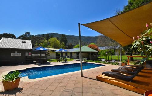 a swimming pool with chairs and an umbrella at Harrietville Hotel Motel in Harrietville