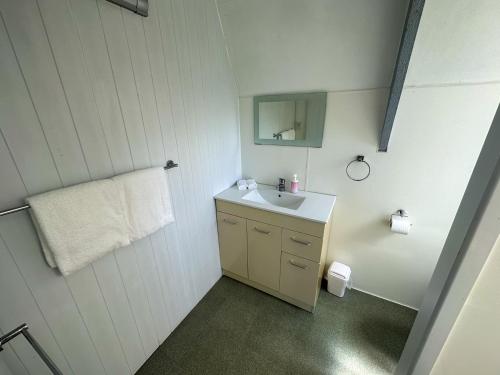 Baño blanco con lavabo y espejo en Pohutukawa Coastal Chalets, en Coromandel