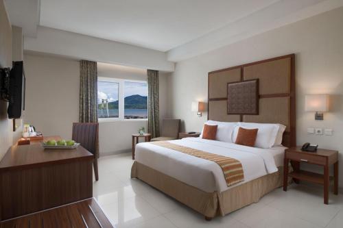 マナドにあるASTON Manado Hotelの大きなベッドとデスクが備わるホテルルームです。