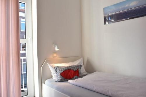 a bedroom with a bed with a red pillow next to a window at Ferienwohnung 206 Juist Strandburg für 5 Personen mit Schwimmbad und Sauna in Juist