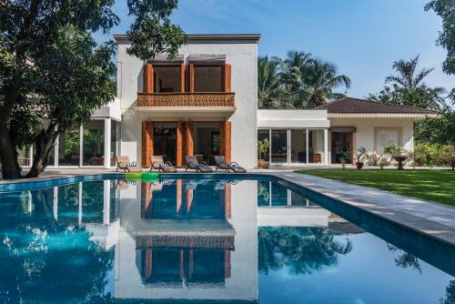 a villa with a swimming pool in front of a house at SaffronStays Hacienda by the Sea, Alibaug in Alibaug