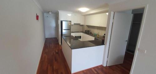 a white kitchen with a refrigerator and a wooden floor at Entire Spacious Apartment in the HEART of Canberra! in Canberra