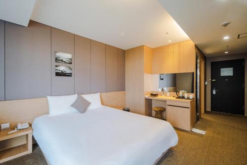 a bedroom with a large white bed and a kitchen at Hotel bridge Seogwipo in Seogwipo