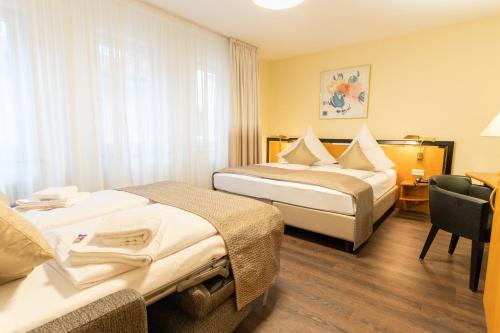 a hotel room with two beds and a chair at Hotel am Stadtgarten in Radolfzell am Bodensee