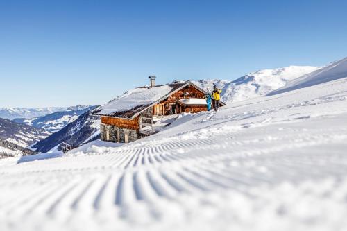 two people standing in the snow in front of a cabin at Hotel Almhof in Hochfugen