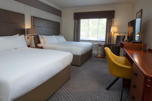 a hotel room with two beds and a desk at Belton Woods Hotel, Spa & Golf Resort in Grantham