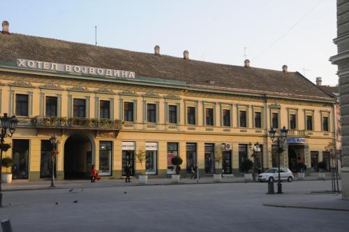 een groot geel gebouw met een auto ervoor geparkeerd bij Hotel Vojvodina in Novi Sad