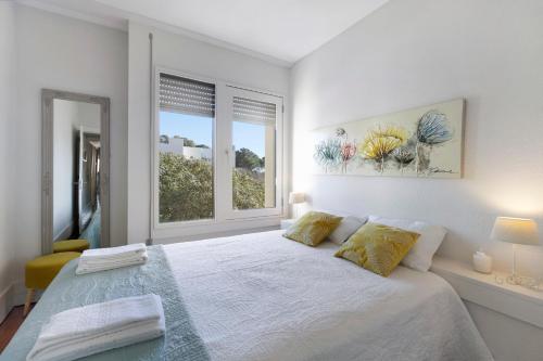 a white bedroom with a large bed with two windows at Apartamento T1 - Tróia Resort in Troia