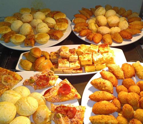 a table full of plates of food with pies and pizzas at Herval Park Hotel in Ponta Porã