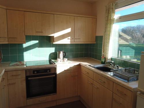 uma cozinha com armários de madeira, um lavatório e uma janela em Glen Dhoo Country Cottages - Meadowview Bungalow em Onchan