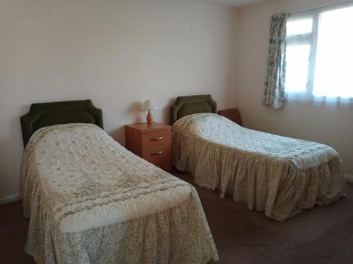 a bedroom with two beds and a dresser and a window at Glen Dhoo Country Cottages - Meadowview Bungalow in Onchan