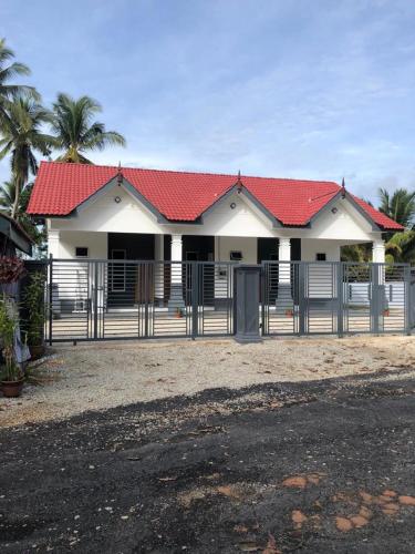 a white house with a red roof and a fence at Roomstay umi in Kemasik