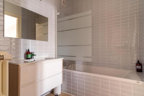 La salle de bains est pourvue d'une baignoire blanche, d'un lavabo et d'une baignoire. dans l'établissement LA SUITE MARCELLIN - Magnifique T3 avec garage et balcon Lyon 7, à Lyon