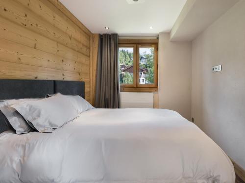 a bedroom with a large white bed with a wooden wall at Appartement rénové 4 pers. au centre de Megève - Balcon, parking, TV, Wifi - FR-1-453-66 in Megève