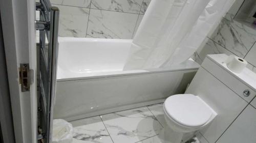 a white bathroom with a toilet and a bath tub at Bethel- beautiful new 1 bed house near Erith station in Erith