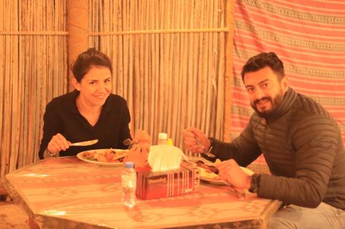 a man and woman sitting at a table eating food at Sands Dream Tourism Camp in Shāhiq