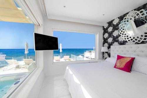 a white bedroom with a large window and a television at Lani's Suites de Luxe - Adults Only in Puerto del Carmen
