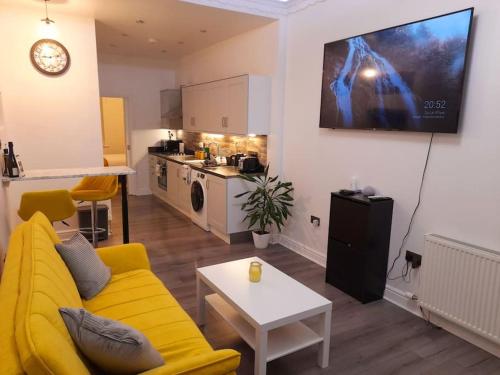 a living room with a yellow couch and a kitchen at Modern flat near city centre. in Edinburgh